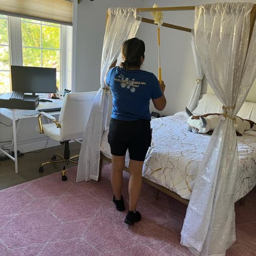 Cleaner making a bed in a bedroom with eco-friendly products in Boston.
